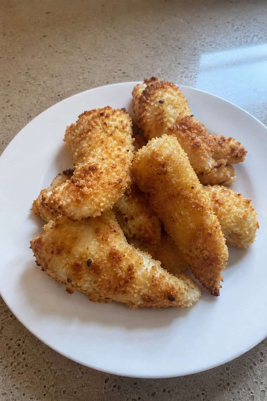 Plate of golden coconut-crusted chicken fingers with dipping sauce and lime wedges on a wooden table.
