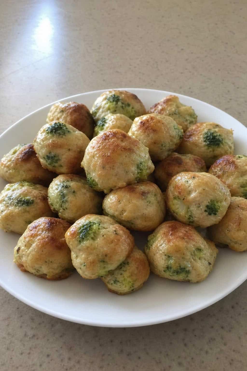 Plate of creamy chicken and broccoli bites on a wooden table with fresh broccoli and dipping sauce in the background.