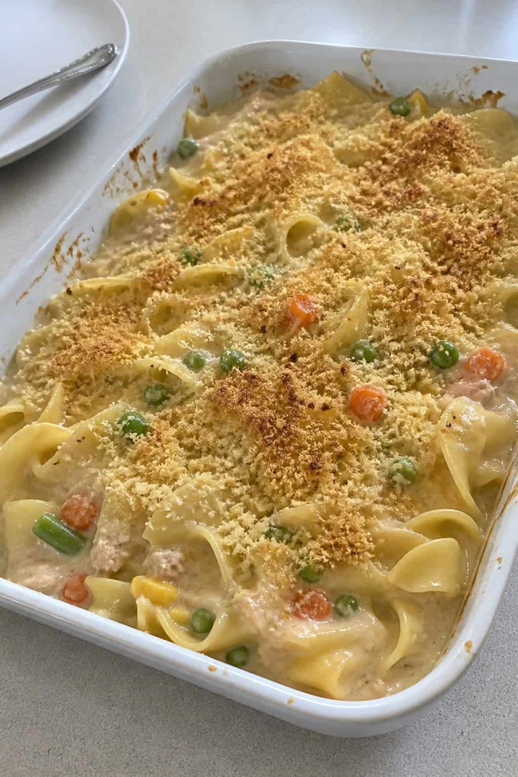 A creamy tuna noodle casserole with mixed vegetables in a ceramic dish on a wooden table.