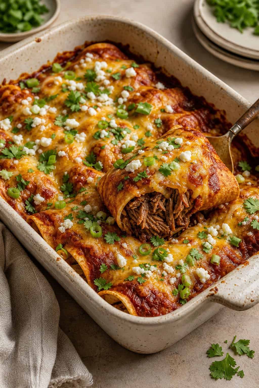 A glass baking dish of shredded beef enchiladas covered in red sauce and bubbling melted cheddar cheese, garnished with fresh cilantro.
