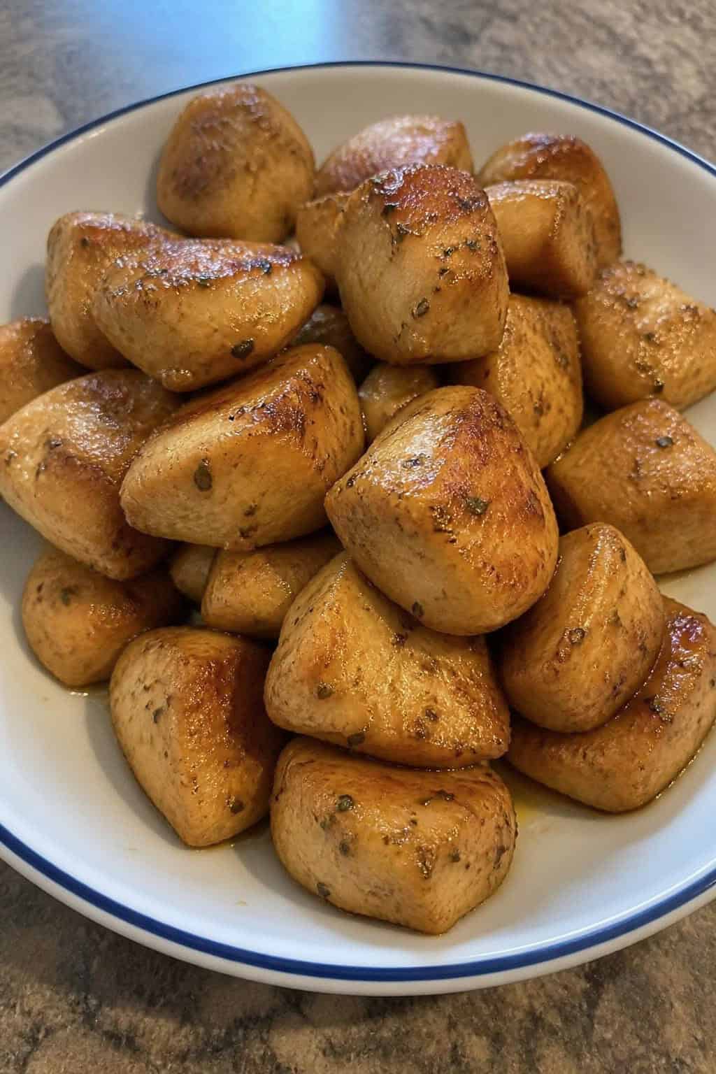 A plate of golden lemon-butter garlic chicken bites garnished with parsley and lemon zest on a wooden table.