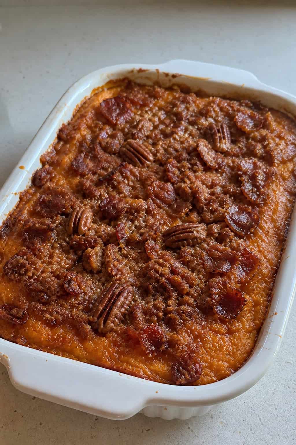 A large baking dish filled with maple-bacon sweet potato casserole on a wooden table with autumn decorations around it.