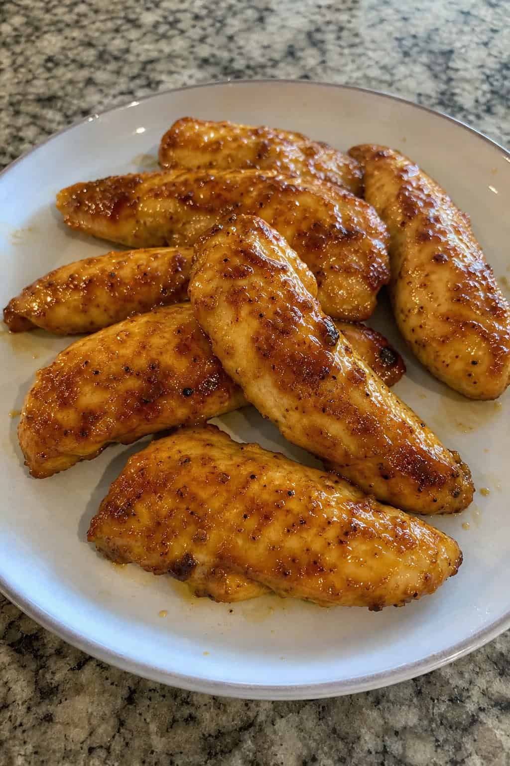 A plate of golden brown maple-mustard chicken tenders garnished with fresh herbs and served with small bowls of dipping sauces on a wooden table.