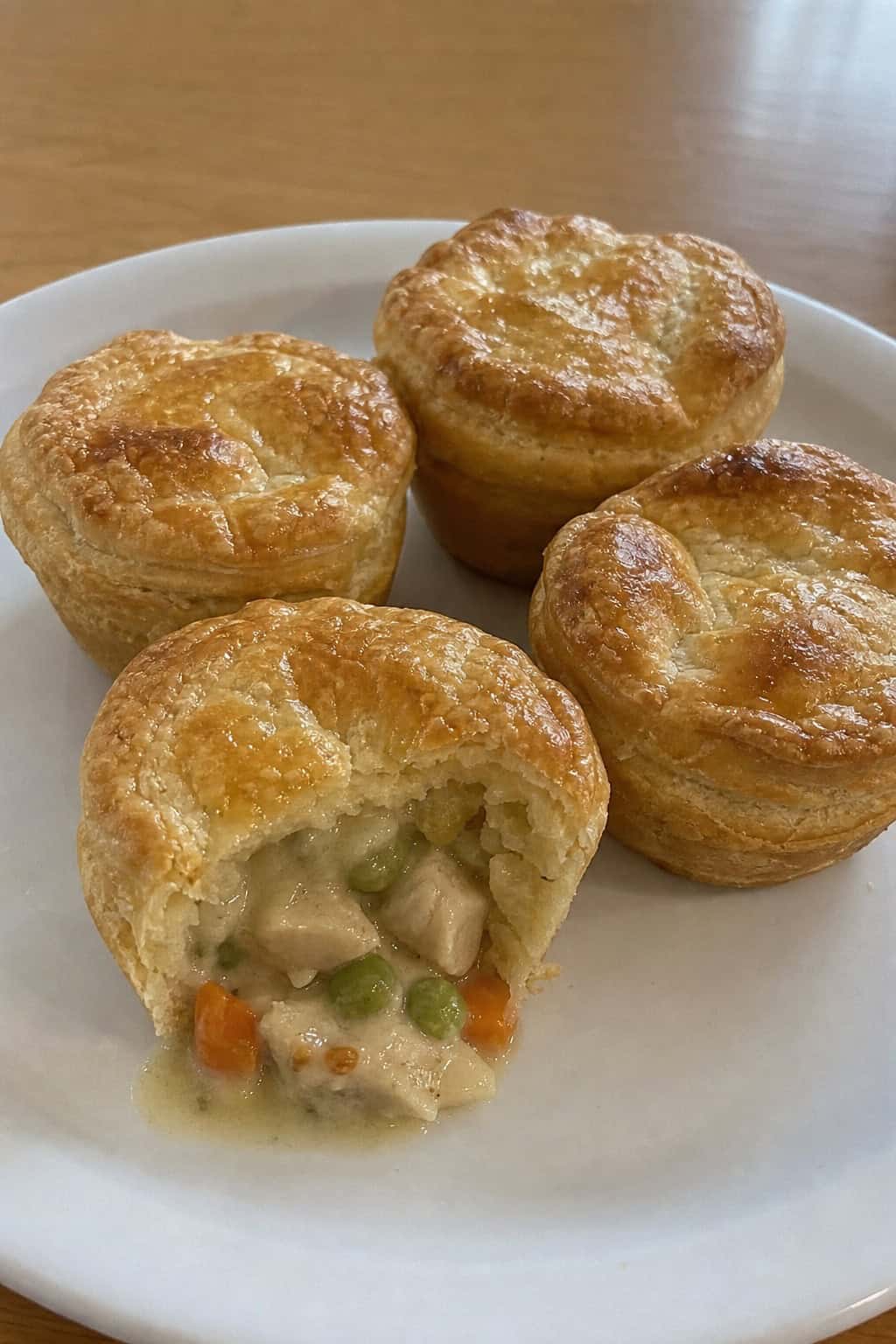 Mini chicken pot pie cups on a wooden board with fresh vegetables around them.