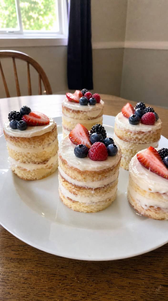A set of mini naked cakes topped with mixed fresh berries arranged on a wooden board.