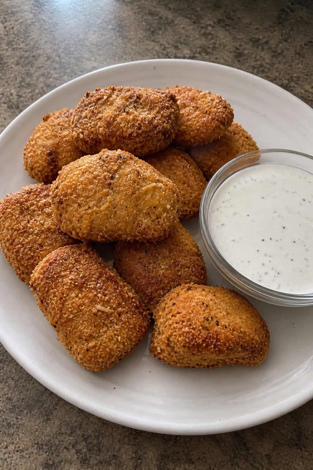 Plate of golden Parmesan ranch chicken nuggets with a bowl of ranch dipping sauce on a wooden table.