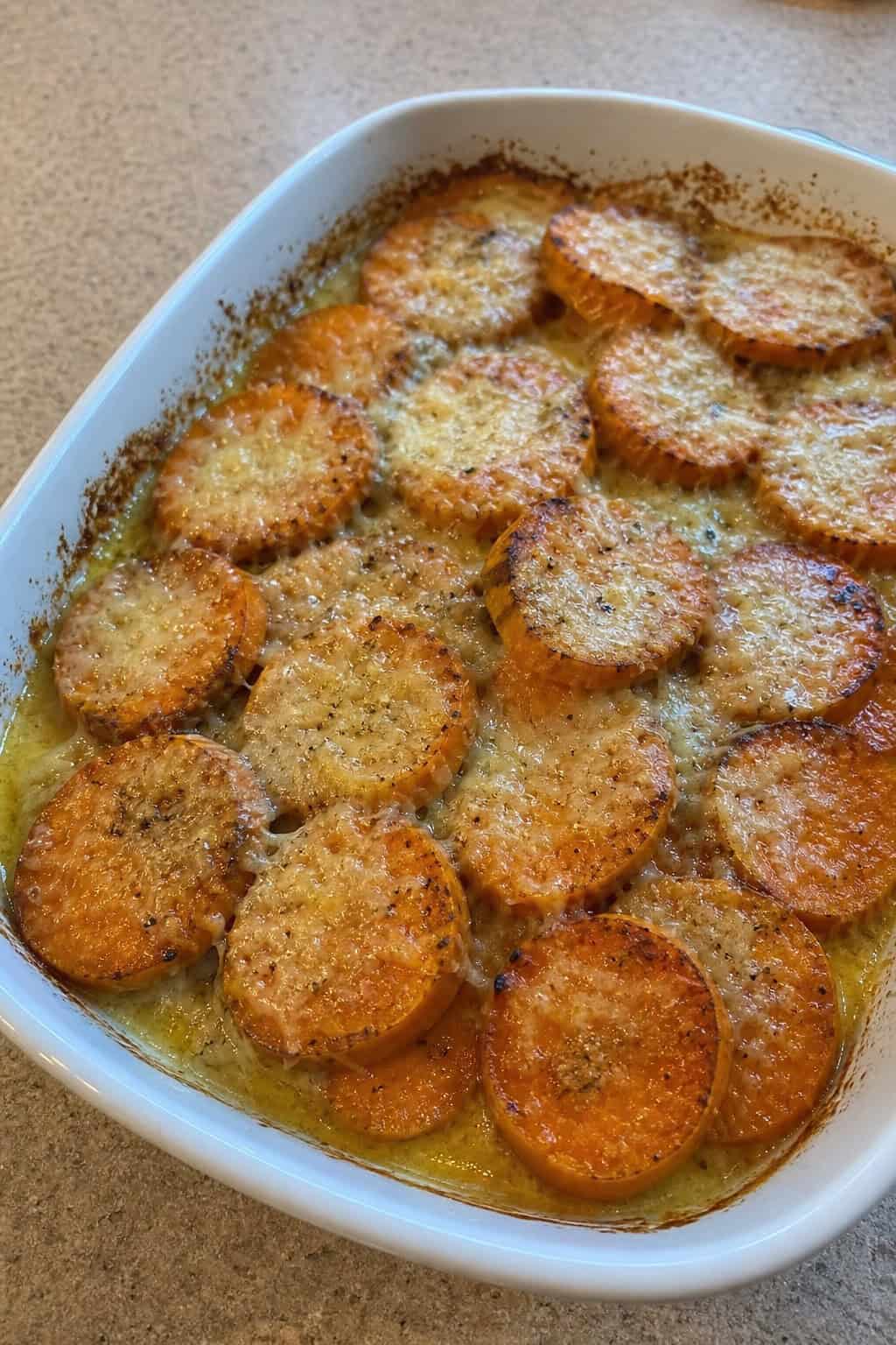 Sweet Potato Casseroles That Feed a Crowd 4 A baked sweet potato casserole topped with melted cheese and fresh herbs in a ceramic dish on a wooden table.
