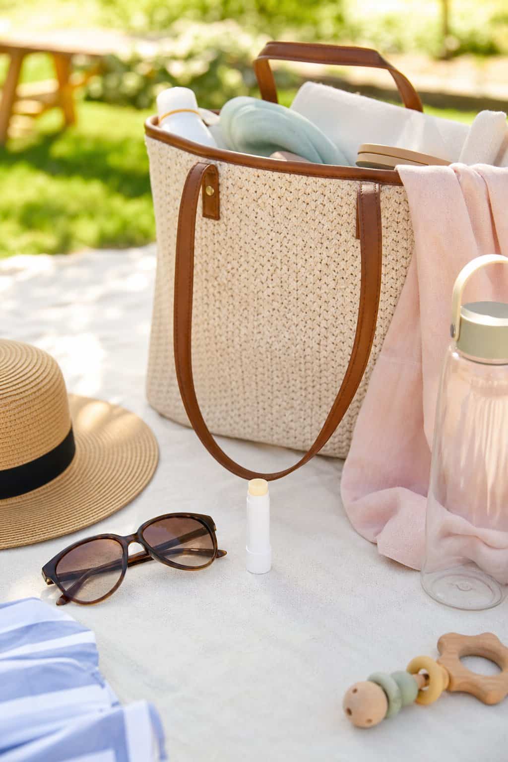 A twist-up SPF lip balm tube resting on top of summer essentials in an open canvas tote bag in natural light.