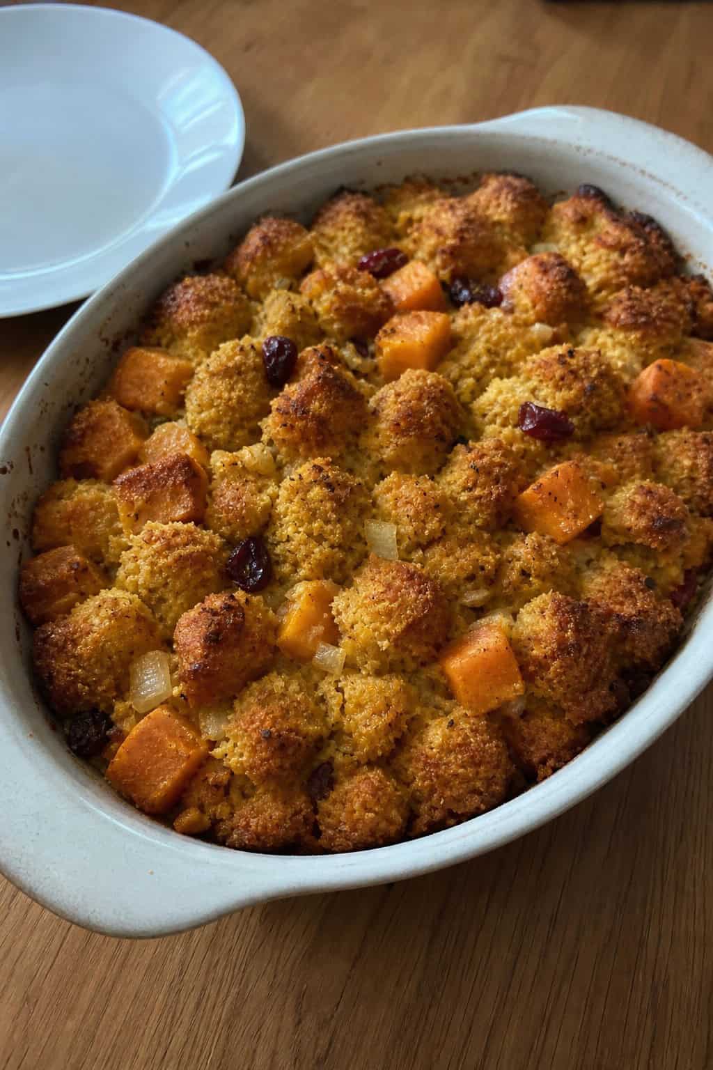 A baked sweet potato and cornbread stuffing casserole in a ceramic dish on a wooden table with autumn decorations around it.