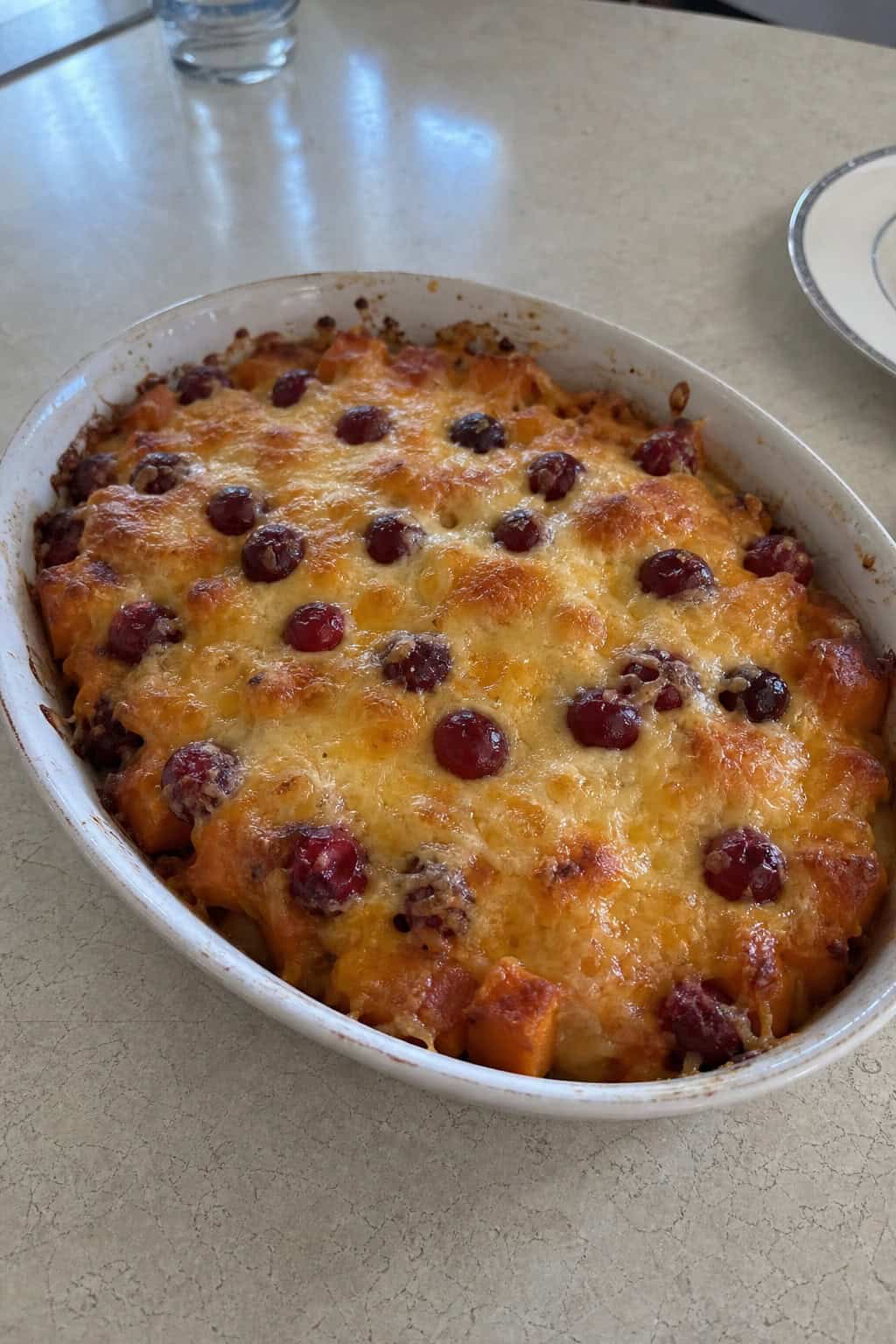 A baked sweet potato and cranberry cheesy casserole in a ceramic dish on a wooden table with autumn decorations.