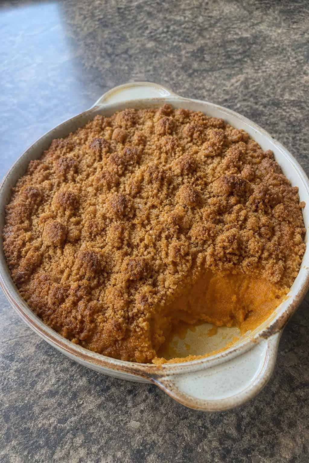 Sweet Potato Casseroles That Feed a Crowd 6 A baked sweet potato casserole with a golden streusel topping in a ceramic dish on a wooden table with autumn decorations.