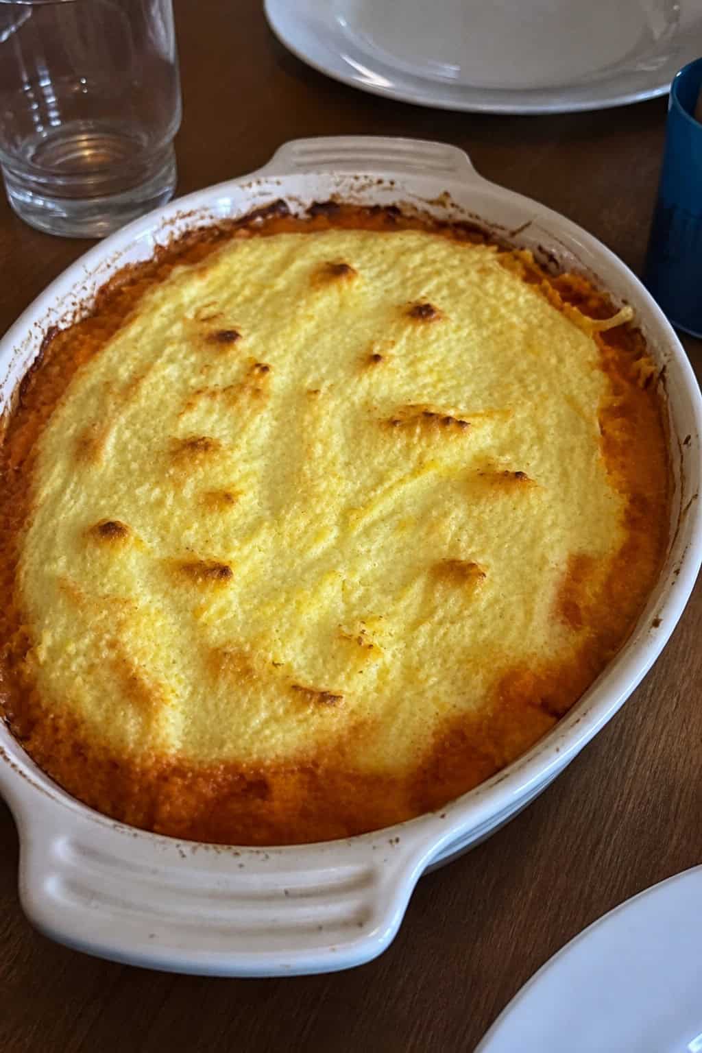 A baking dish filled with sweet potato casserole topped with a creamy lemon-ricotta layer on a wooden table with autumn decorations around it.