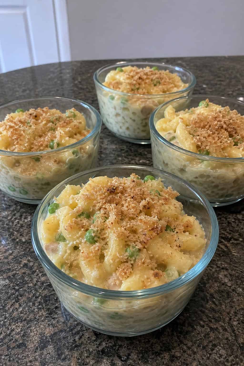 Single-serve tuna noodle casserole cups on a wooden table with fresh ingredients around them.