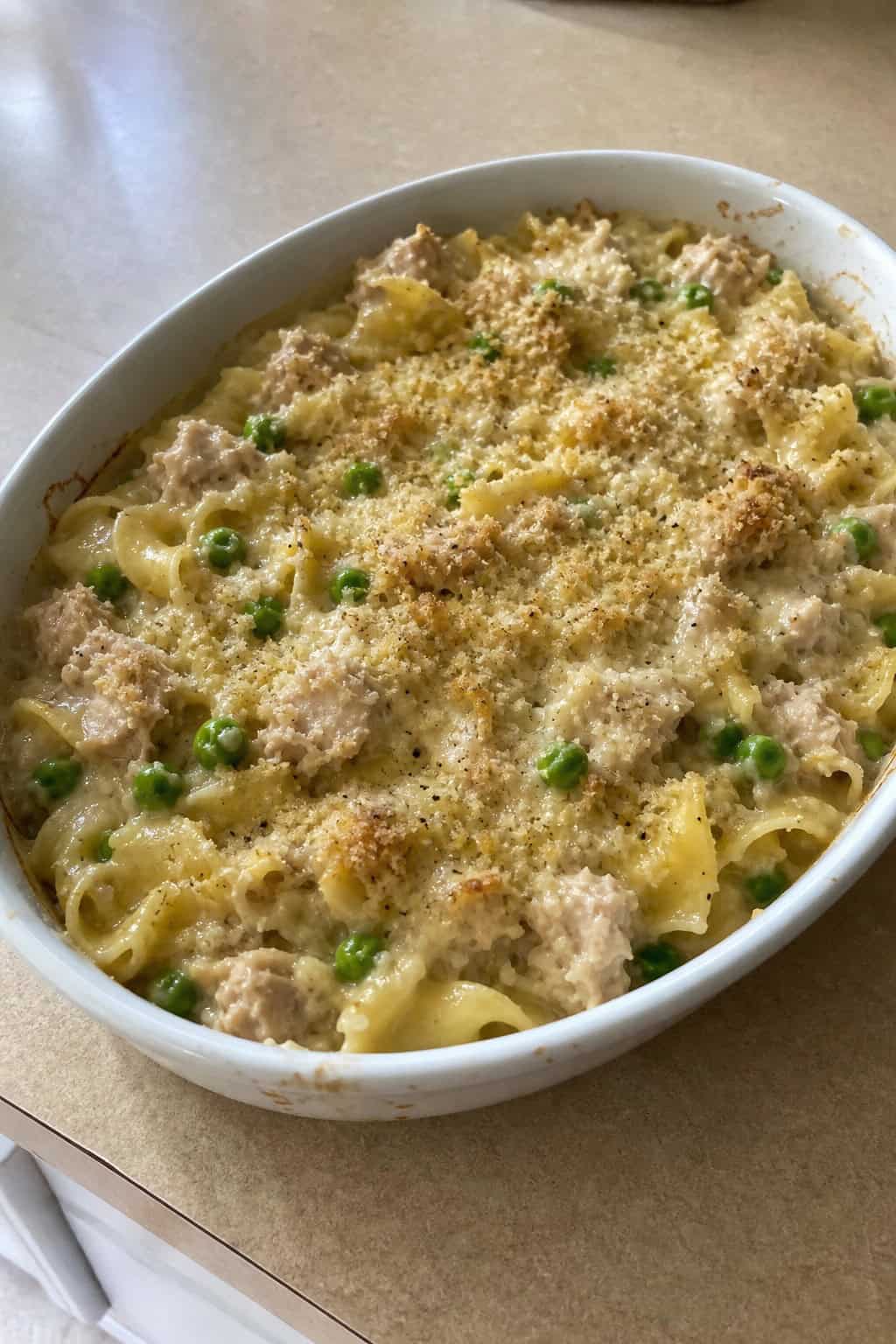 A baked tuna noodle casserole with creamy sauce and peas in a ceramic dish on a wooden table.