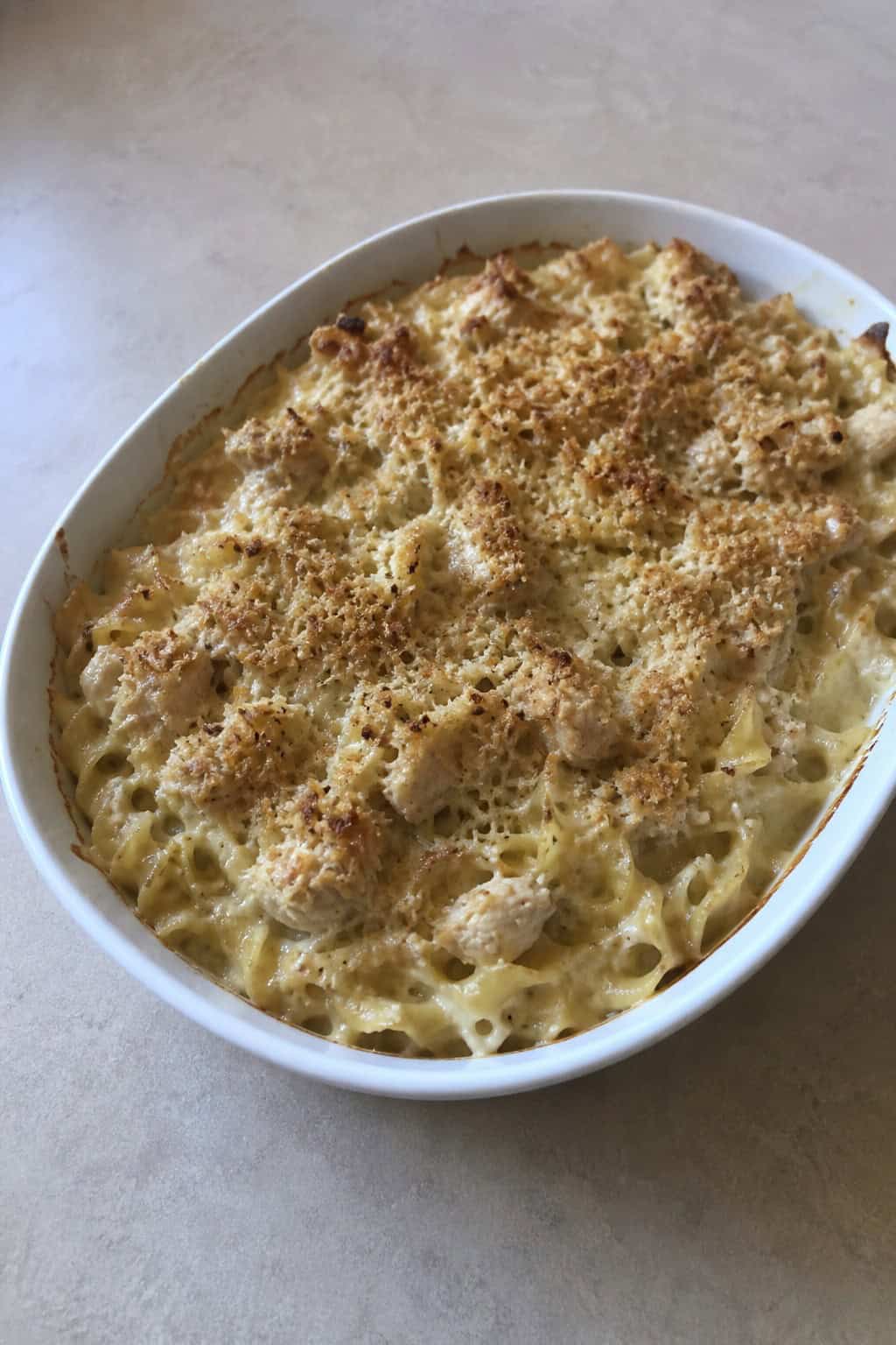 A baked tuna noodle casserole topped with caramelized onions and thyme in a ceramic dish on a wooden table.