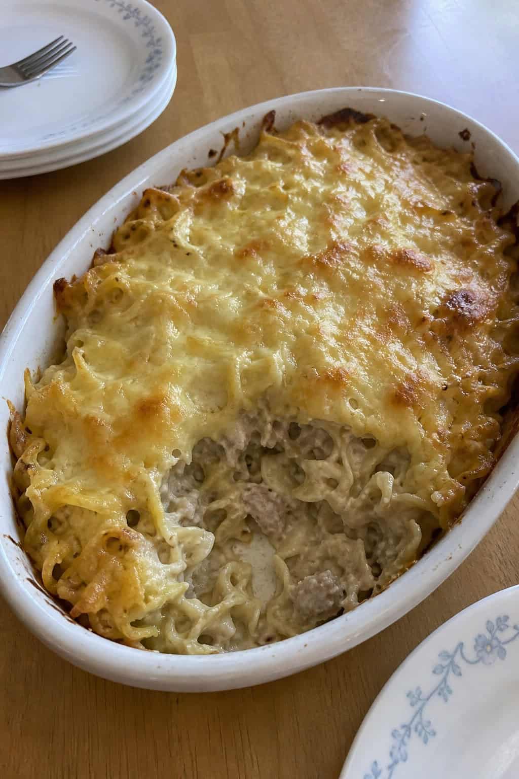 A baked tuna noodle casserole topped with melted cheese and garnished with parsley on a wooden table.