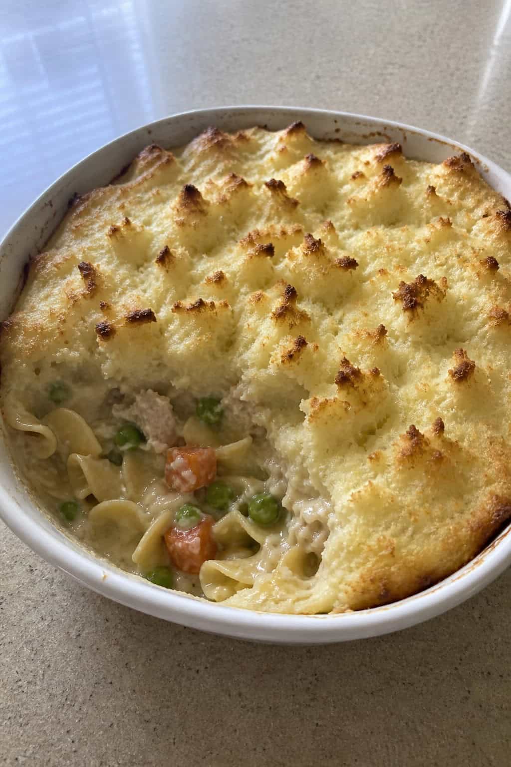 A baked tuna noodle casserole topped with mashed potatoes in a ceramic dish on a wooden table.