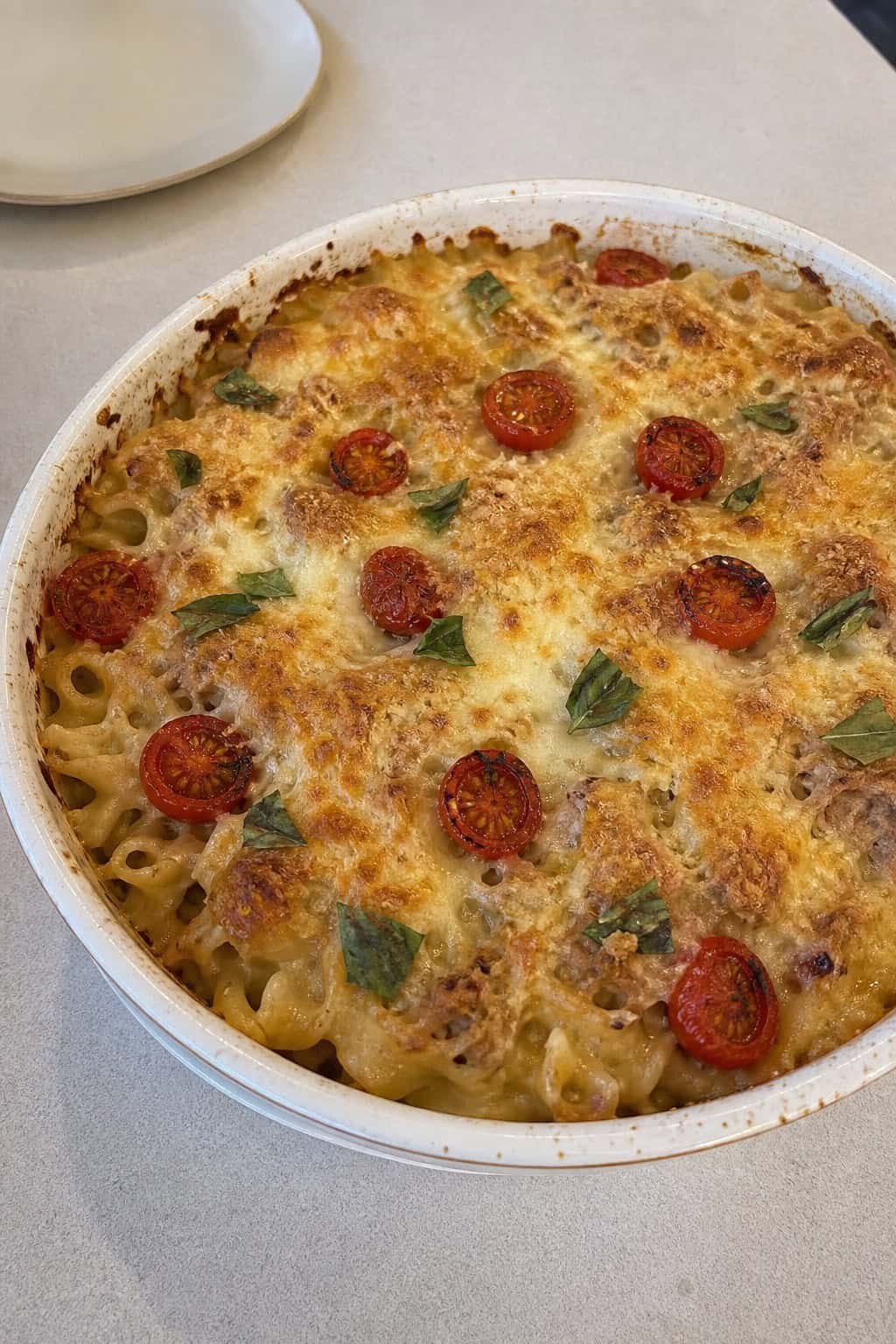 A baked tuna noodle casserole with roasted cherry tomatoes and fresh basil on a kitchen table.