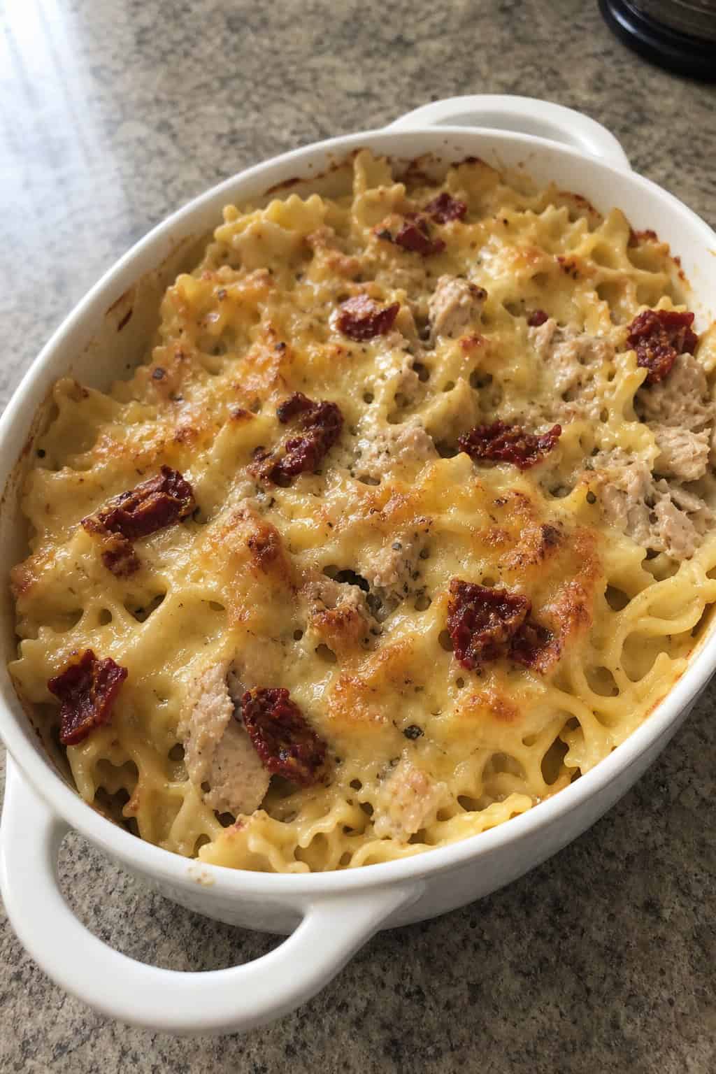 A baked tuna noodle casserole with sun-dried tomatoes and basil in a ceramic dish on a wooden table.