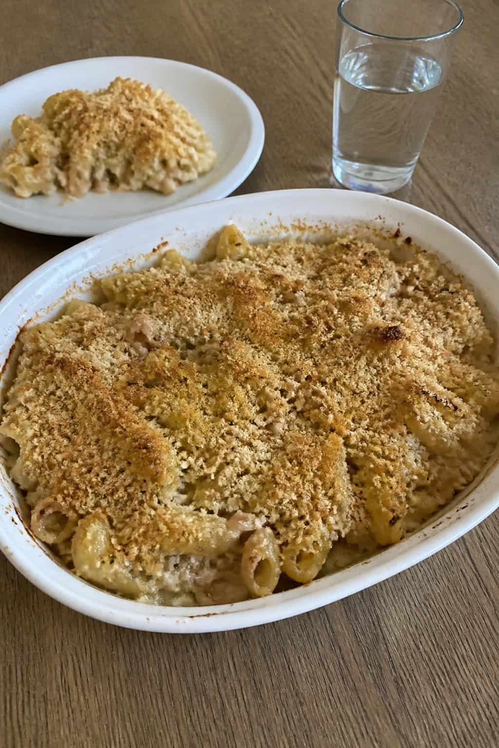 A baked tuna noodle casserole with a golden crust in a ceramic dish on a wooden table, garnished with fresh herbs.