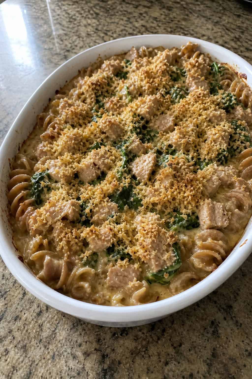 25 Tuna Noodle Casseroles for Busy Weeknights 10 A baked tuna noodle casserole with whole wheat pasta and spinach in a ceramic dish on a wooden table.