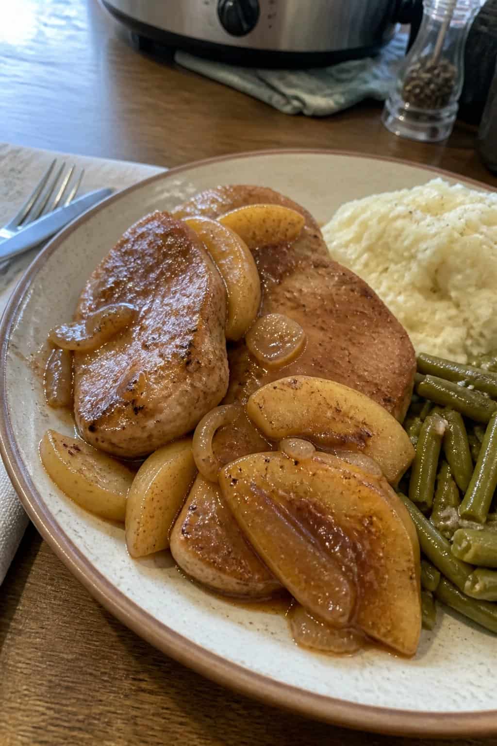 A plate of apple cinnamon pork chops with apple slices and a simple side dish on a kitchen table.