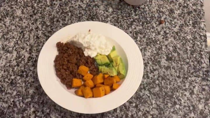 The Viral Hot Honey Beef Protein Bowl 5 A white bowl holds seasoned ground beef, cubed sweet potatoes, avocado slices, and a scoop of cottage cheese arranged together.