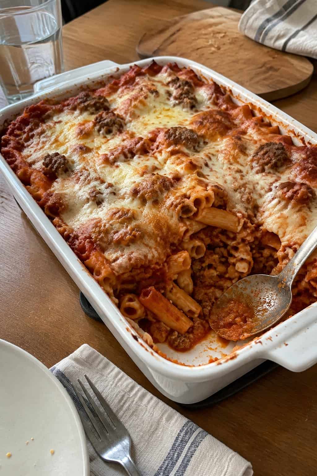 A dish of baked ziti with Italian sausage, tomato sauce, and melted cheese on a kitchen table.