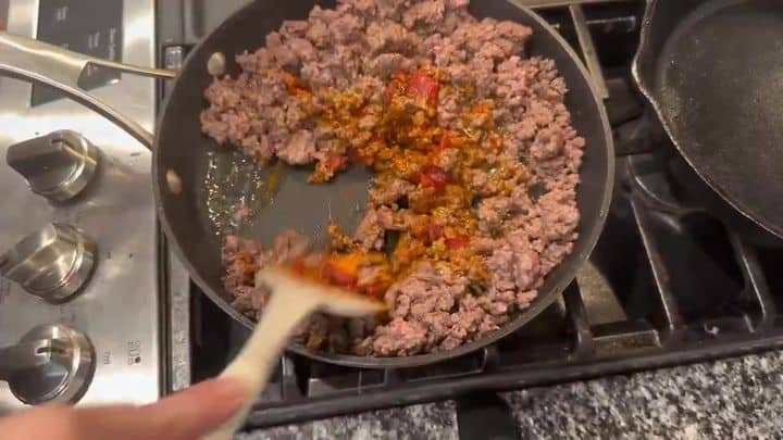The Viral Hot Honey Beef Protein Bowl 4 Ground beef seasoned with taco spices is being cooked and stirred in a skillet on the stovetop.