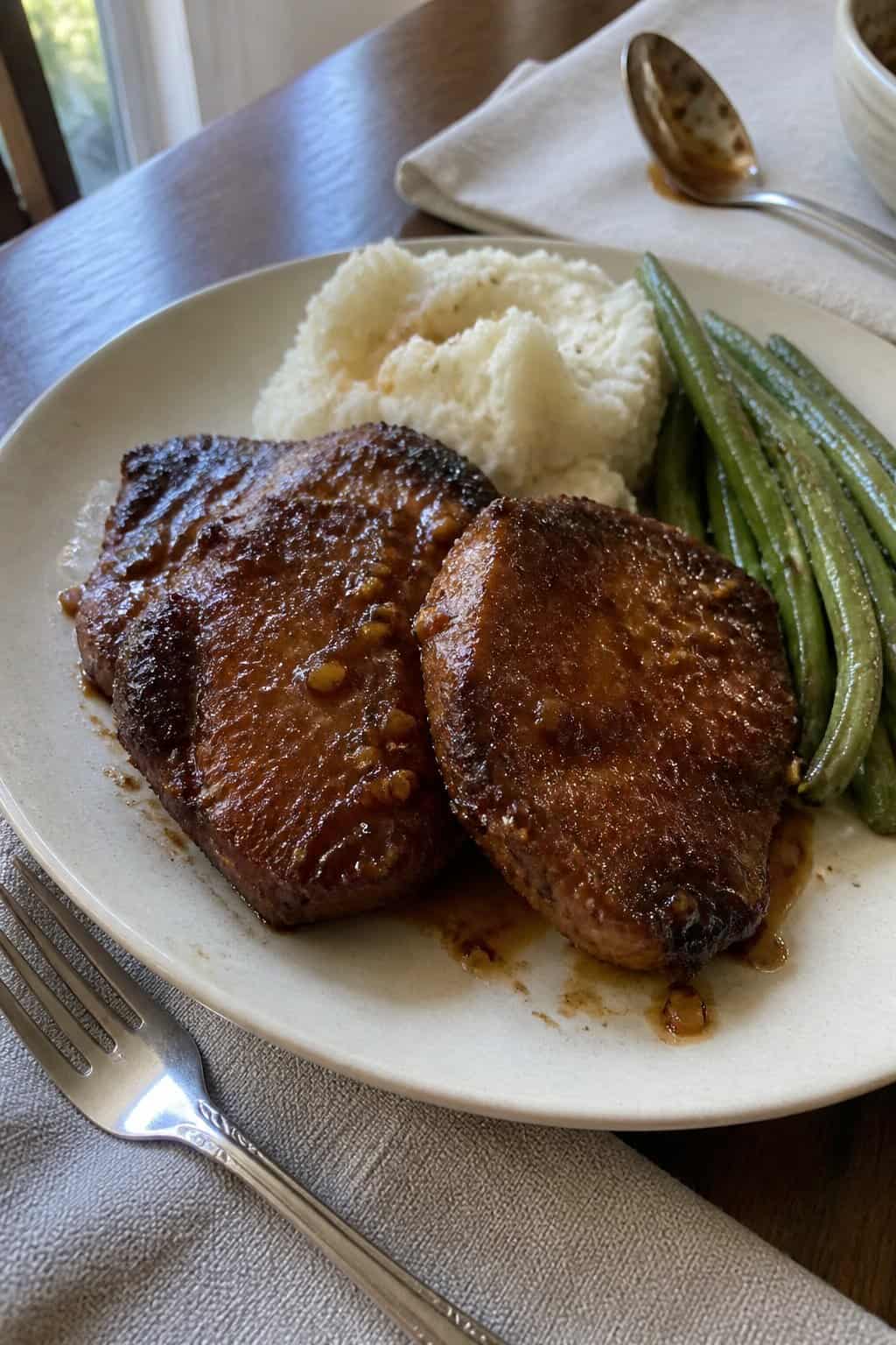 Brown sugar garlic pork chops served with mashed potatoes and green beans on a dinner plate.