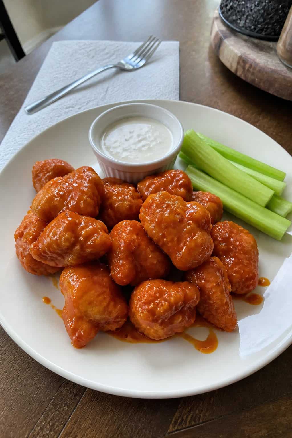 20 Copycat Chicken Recipes for Restaurant Cravings at Home 7 A plate of saucy boneless chicken wings with ranch dressing and celery sticks on a kitchen table.