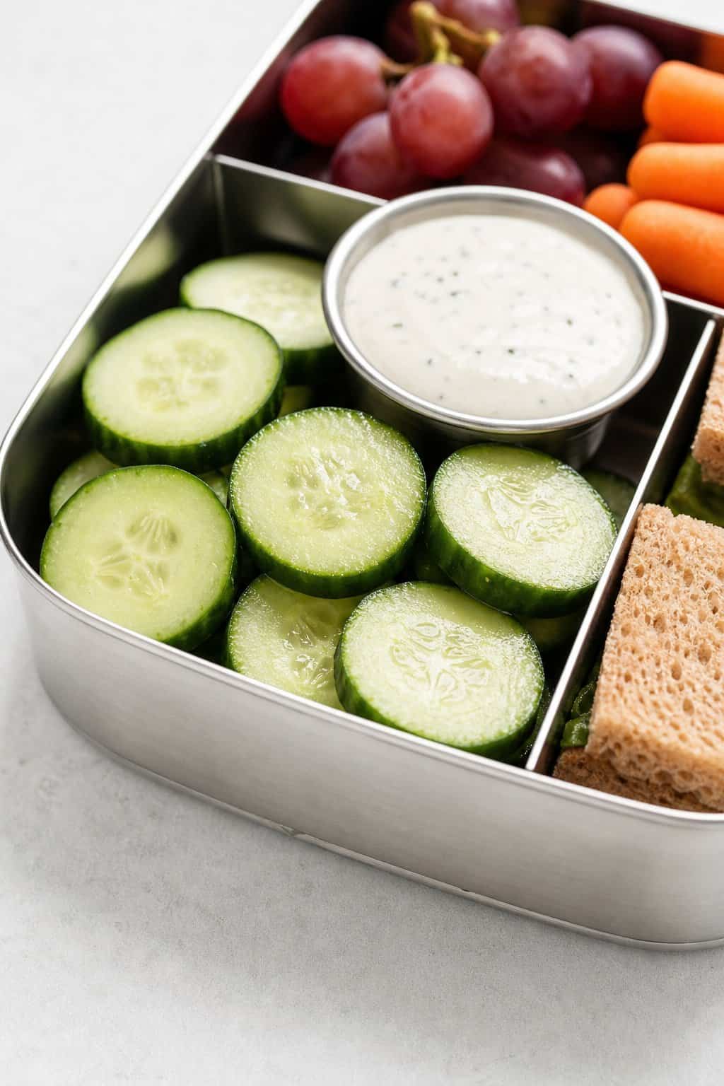 16 Easy Lunchbox Sides Kids Will Eat 5 Cucumber slices arranged in a lunchbox compartment with a small cup of ranch dip.