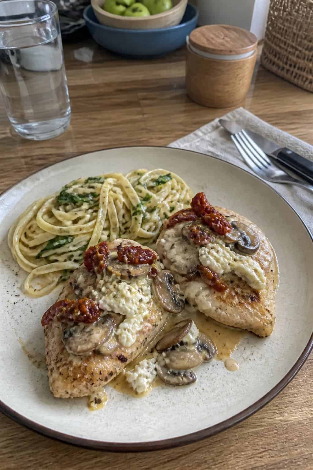 20 Copycat Chicken Recipes for Restaurant Cravings at Home 15 A plate of grilled chicken topped with creamy sauce, mushrooms, sun-dried tomatoes, and goat cheese, served with pasta in a home kitchen.