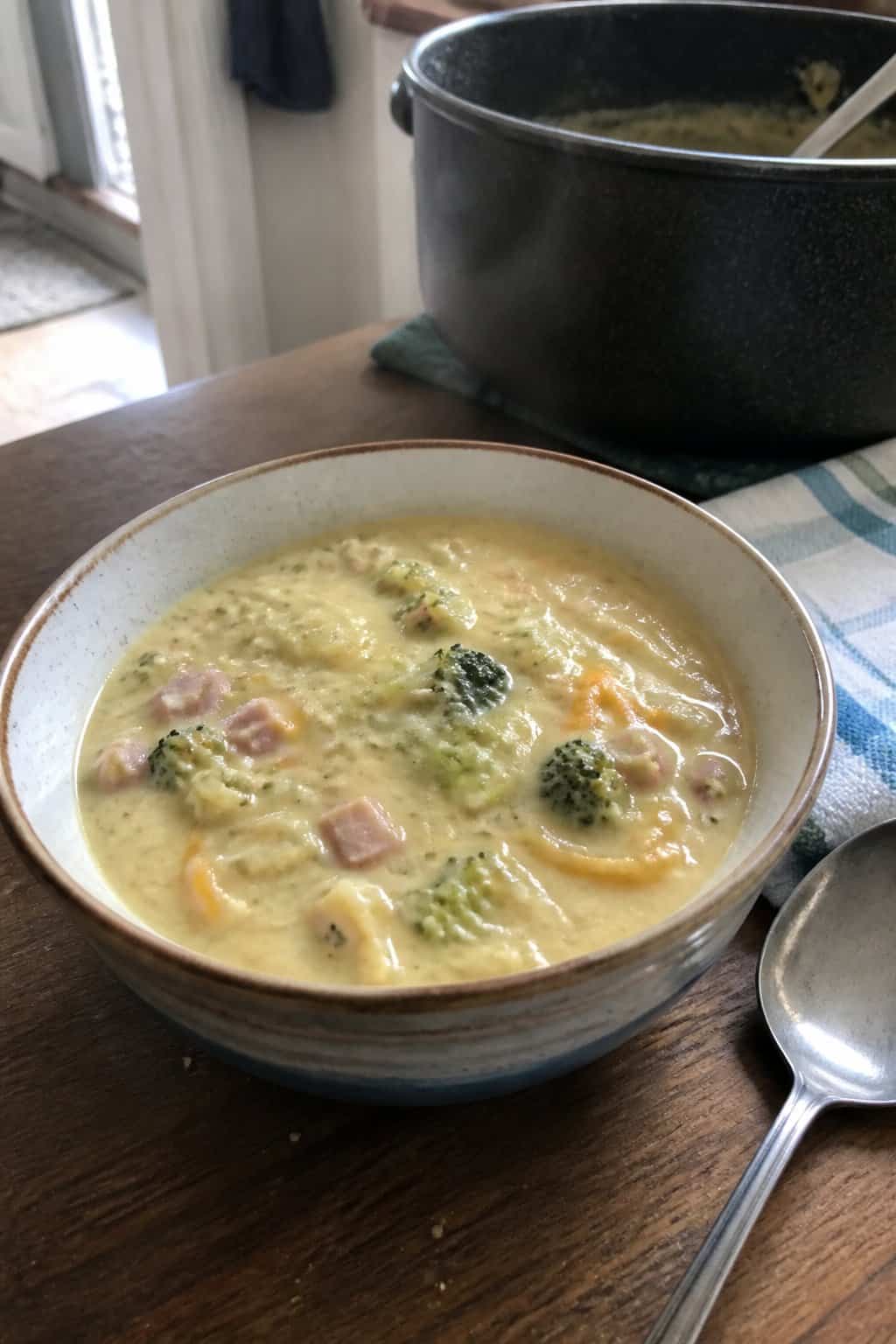 Ham Soup Recipes for Chilly Nights 10 A bowl of creamy ham and broccoli soup sits on a kitchen table beside a spoon and napkin.