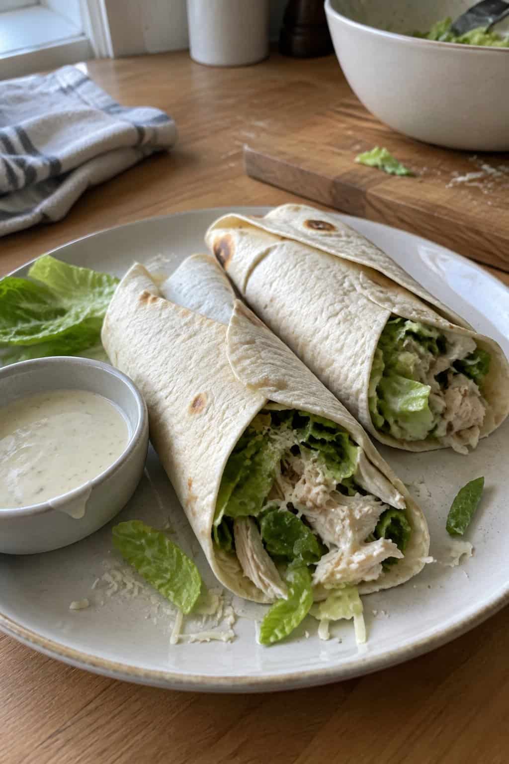 Chicken Caesar wraps with shredded chicken and lettuce arranged on a plate in a home kitchen.