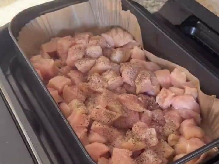 Diced chicken pieces are cooking in the air fryer basket lined with parchment paper.