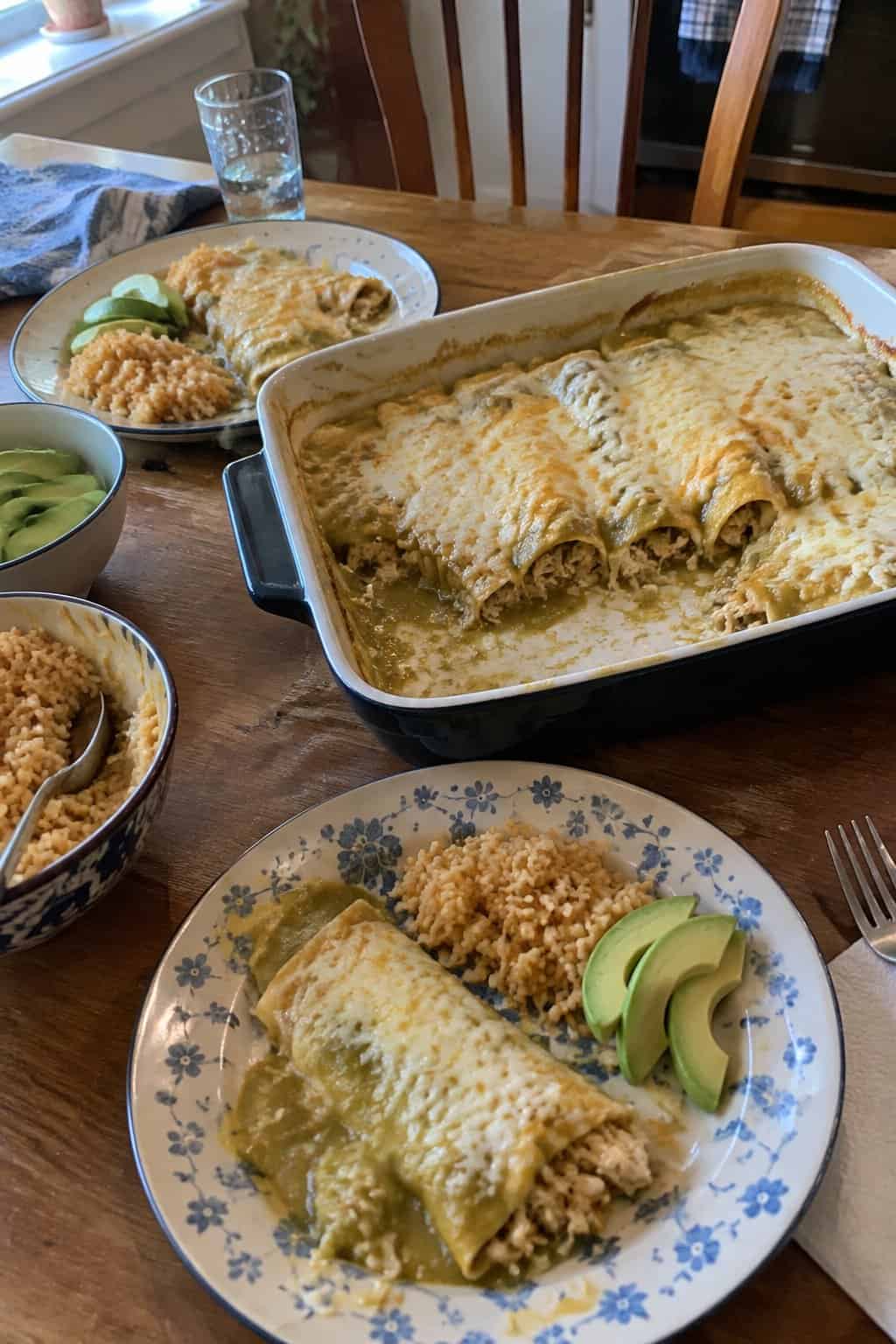 Chicken enchiladas covered in green chile sauce and melted cheese, served with rice and avocado.