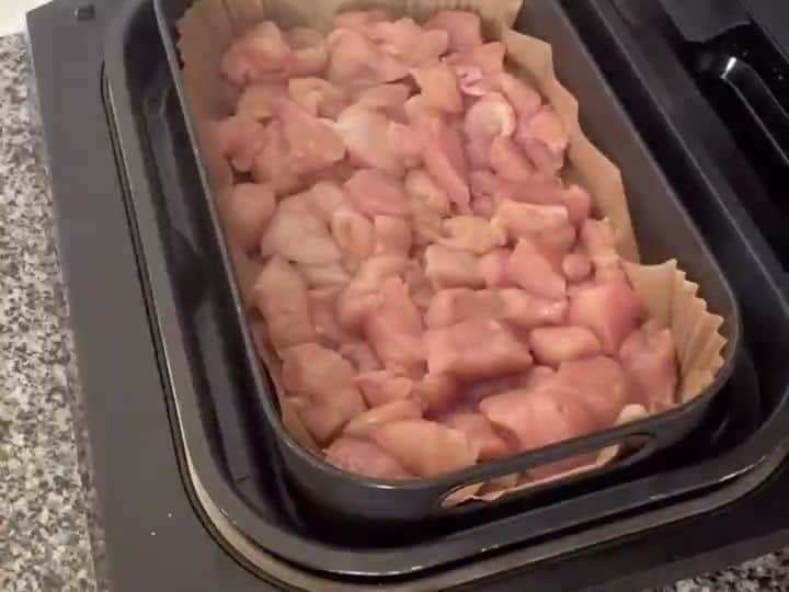 Easy Chicken Fried Rice 4 Raw bite-sized chicken pieces sit in a black air fryer basket lined with parchment paper.