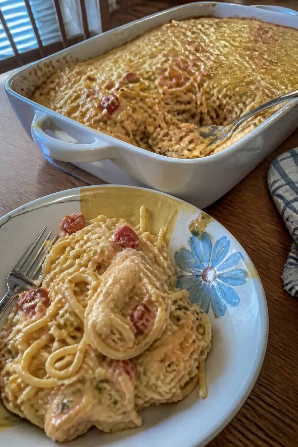A creamy chicken spaghetti casserole with tomatoes and green chilies served from a white baking dish.