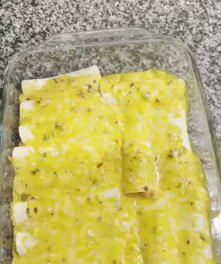 Baked chili cheese enchiladas covered in melted queso and cheese in a glass casserole dish