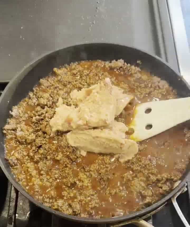 Seasoned ground beef, red enchilada sauce and refried beans being mashed together in a skillet