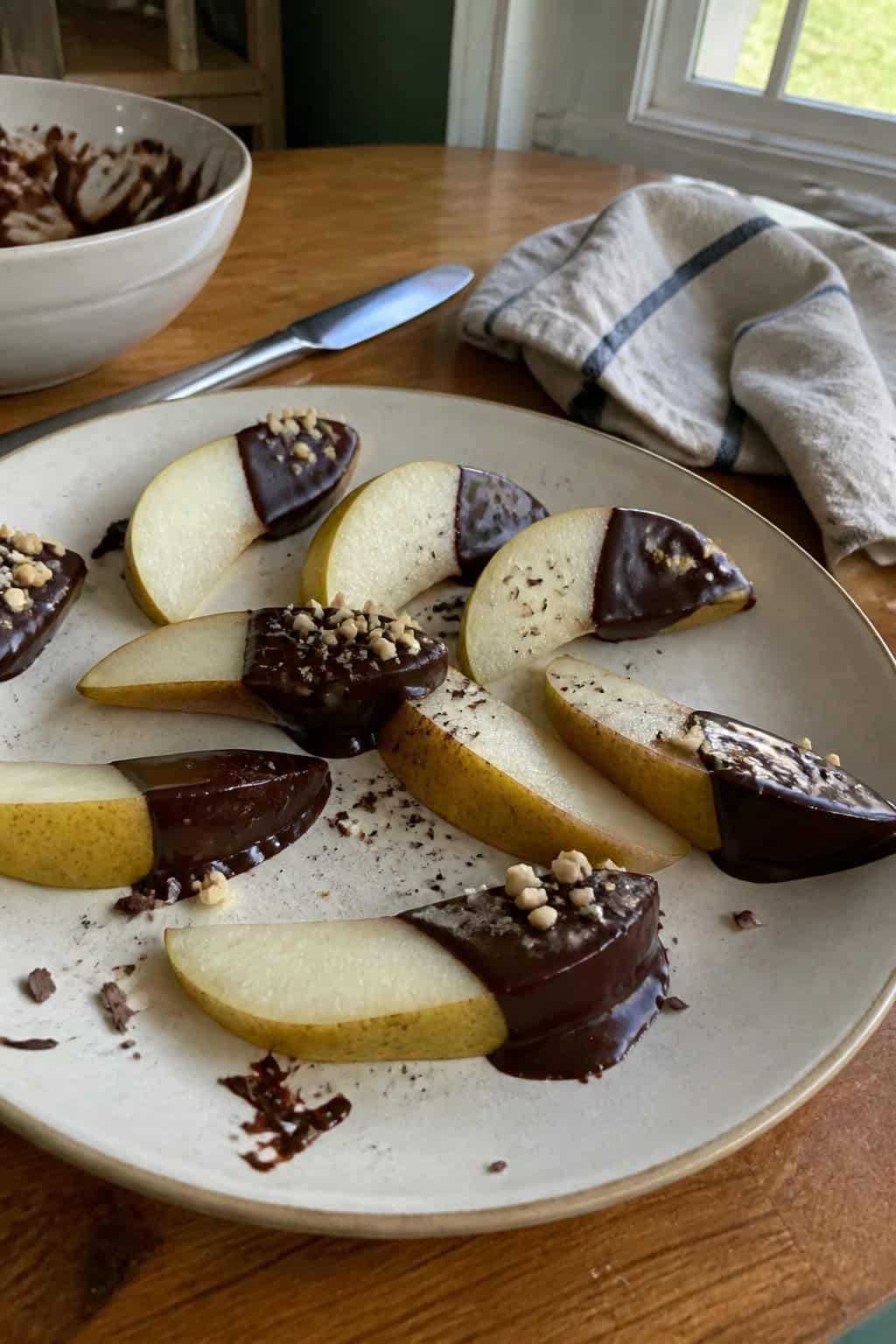 Chocolate-dipped pear slices arranged on a plate on a kitchen table.