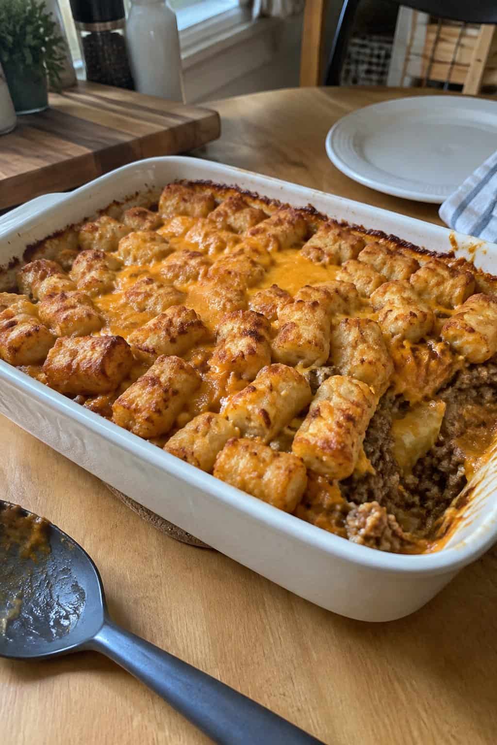 A homemade beef and cheddar casserole topped with golden tater tots in a baking dish on a kitchen counter.