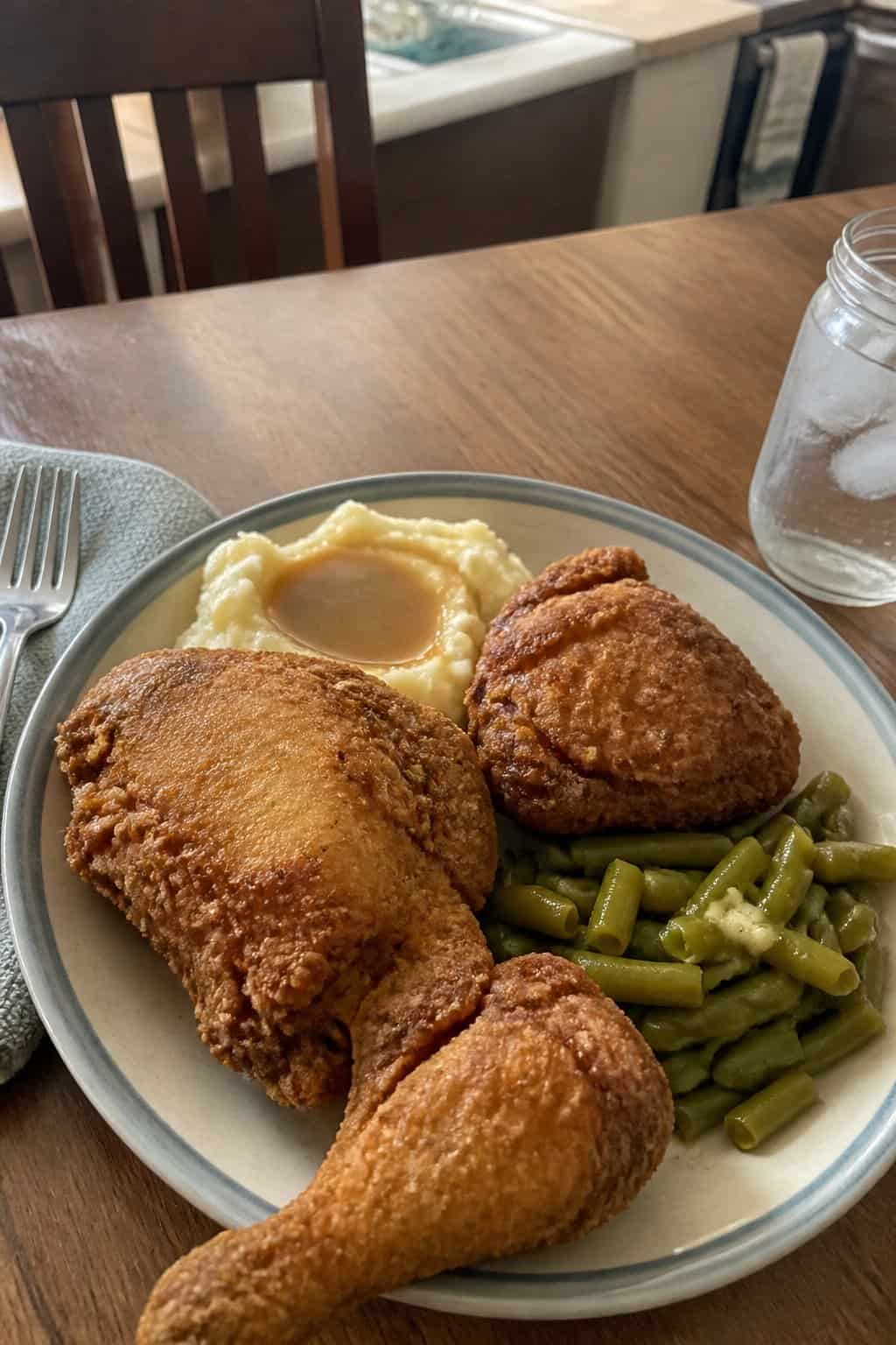 20 Copycat Chicken Recipes for Restaurant Cravings at Home 8 A plate of homemade fried chicken with mashed potatoes, gravy, and green beans on a kitchen table.