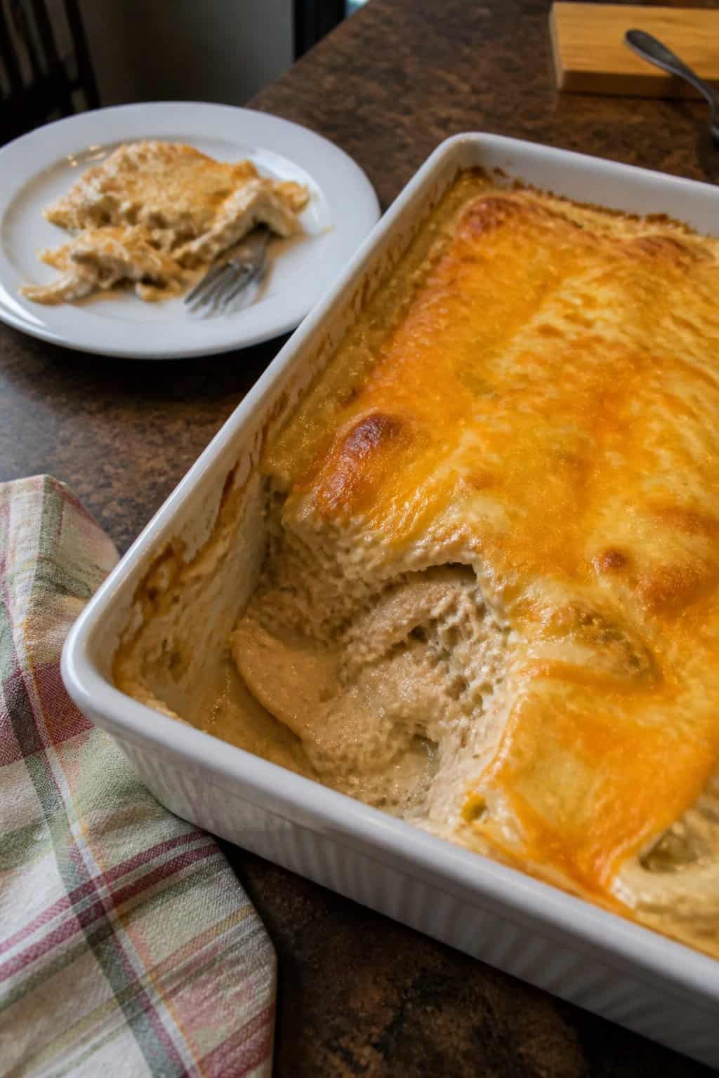 A serving of creamy chicken enchilada casserole in a baking dish on a kitchen table.