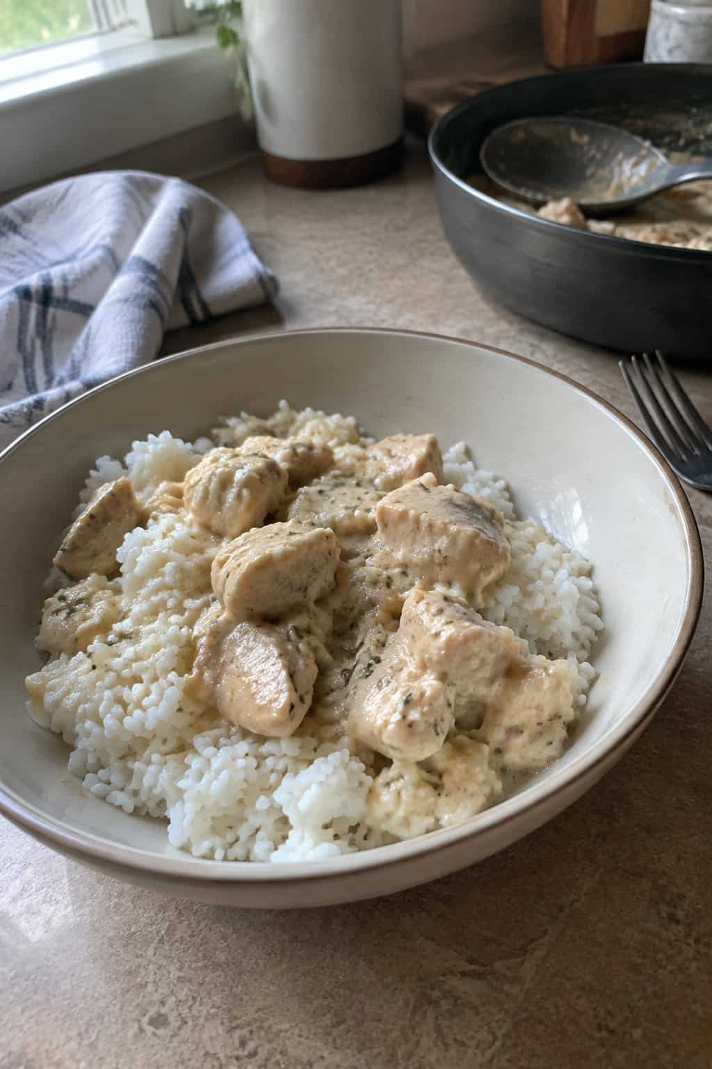 A bowl of creamy chicken and rice sits on a kitchen table near a window.