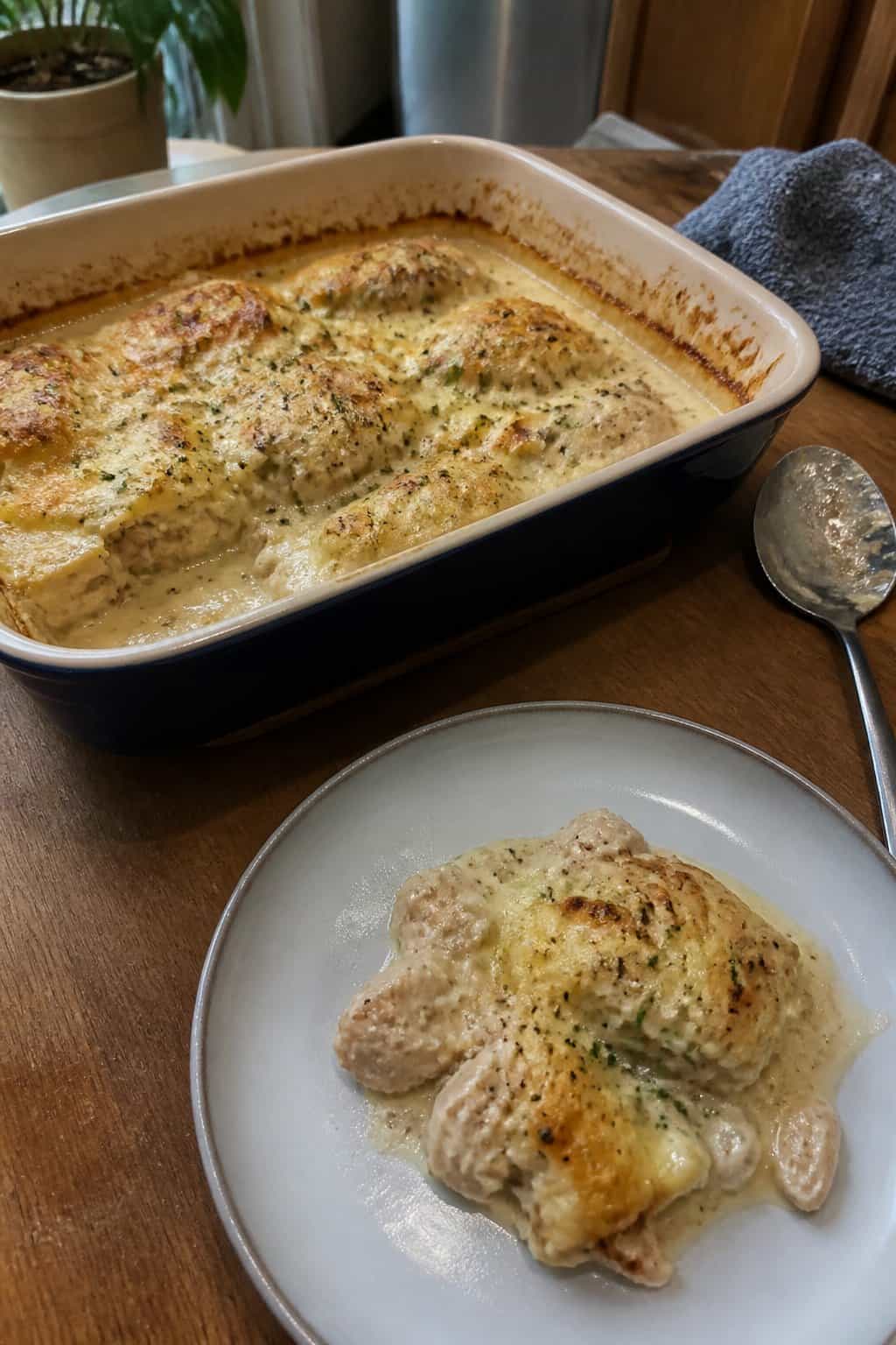A creamy garlic Parmesan chicken bake with browned cheese sits in a ceramic casserole dish on a kitchen table.