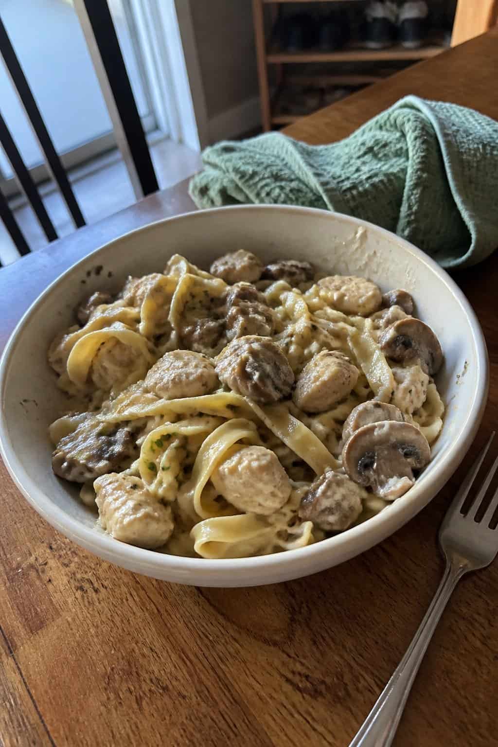 A homemade dish of creamy chicken, mushrooms, and noodles served in a ceramic bowl on a kitchen table.