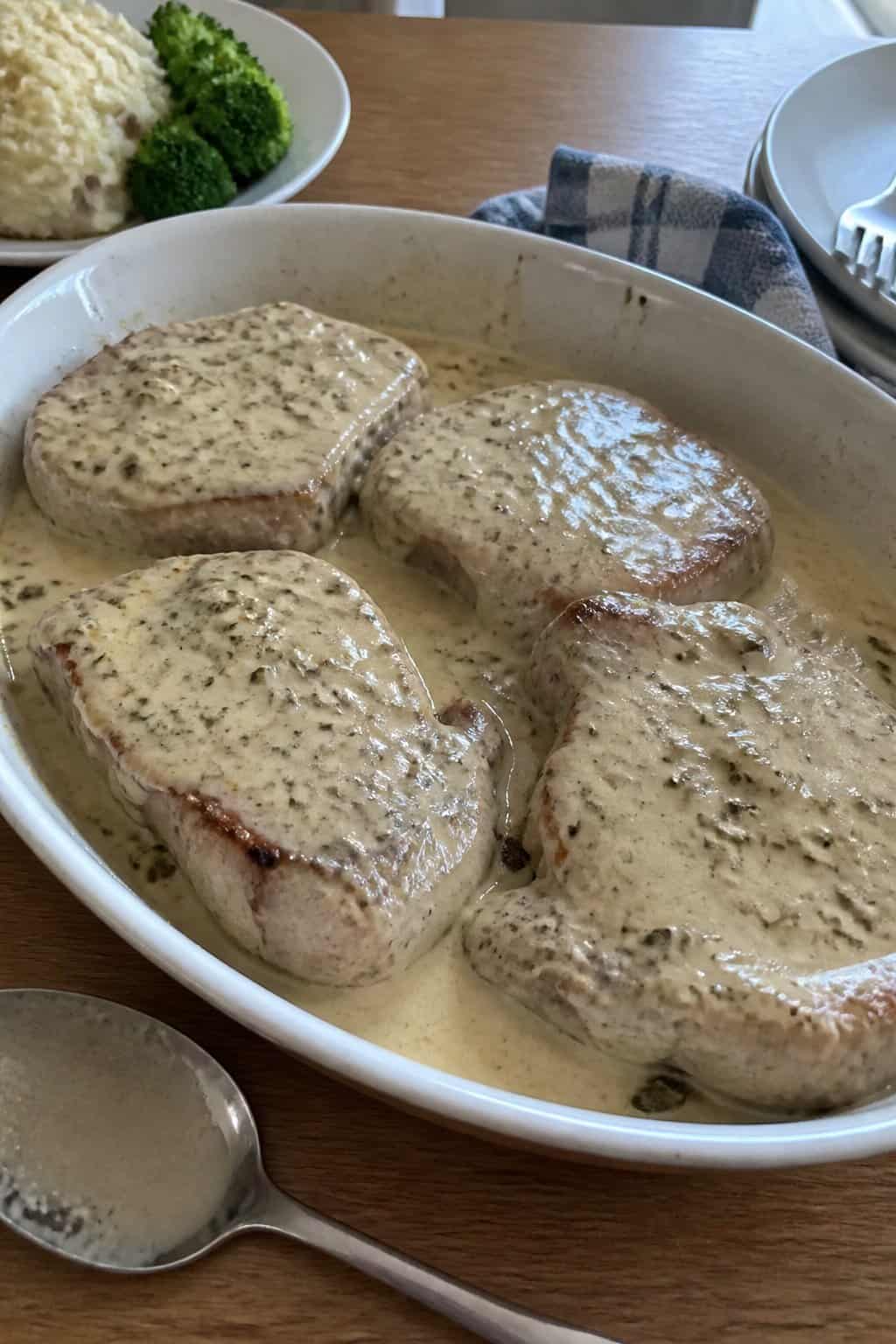 A dish of creamy ranch pork chops served with a simple side of vegetables on a kitchen table.