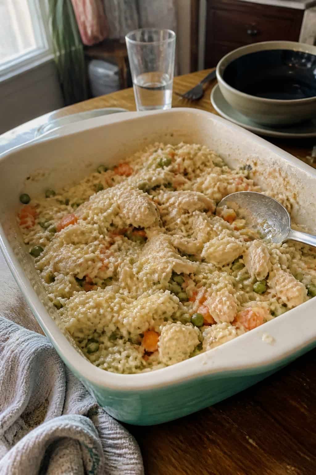 A casserole dish of chicken, rice, peas, and carrots on a kitchen table.